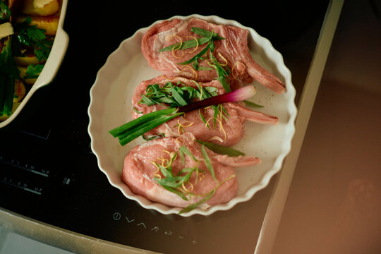 A white dish with raw lamb chops garnished with fresh herbs on an induction cooktop.