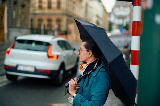 Adult person waiting to cross the street on a cloudy day, holding an open black umbrella.