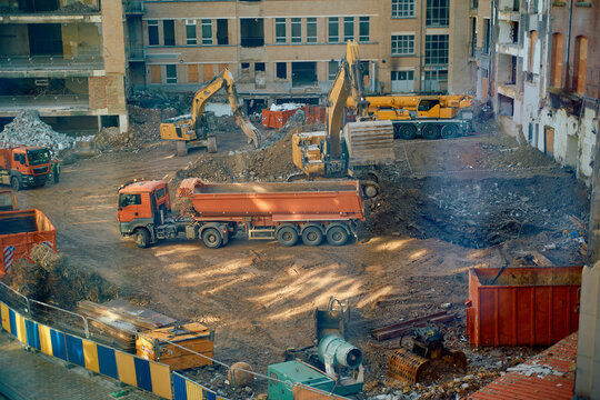 Construction site with excavators and trucks amidst demolition debris, viewed from above.