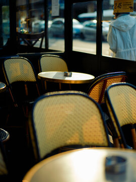 Sunlight filters through a window illuminating an empty cafe interior with round tables and wicker chairs, creating a warm and inviting atmosphere.