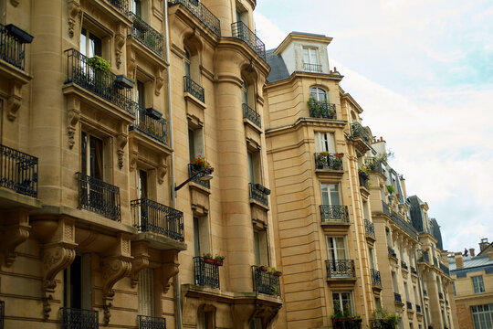 Elegant Parisian building facade with balconies and lush flower boxes against a cloudy sky.