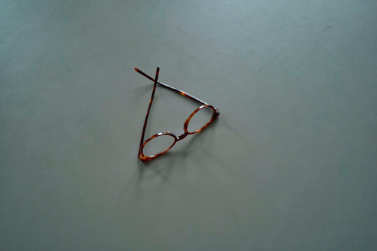 A pair of round-framed glasses lying on a grey surface.