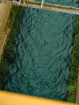A person bungee jumping from a high bridge over a river surrounded by greenery.