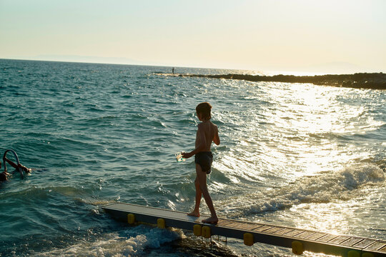 A person stands on a dock overlooking the choppy ocean waves at sunset.