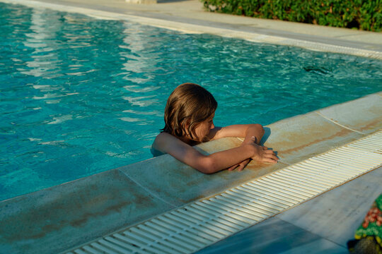 Child relaxing on the edge of a swimming pool during a sunny day.