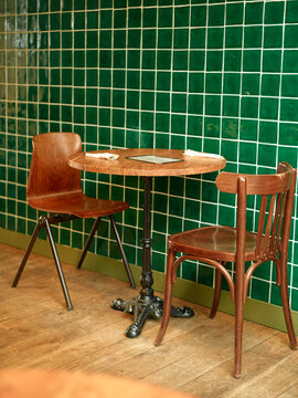 Vintage wooden chairs and round table against a green tiled wall in a cozy corner.