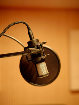 Condenser microphone with pop filter attached to a boom arm set against a blurred warm background.