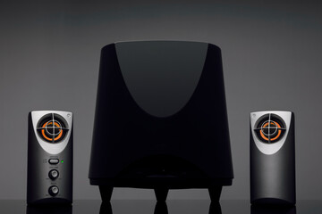 Black desktop speaker system with orange details against a gray background.