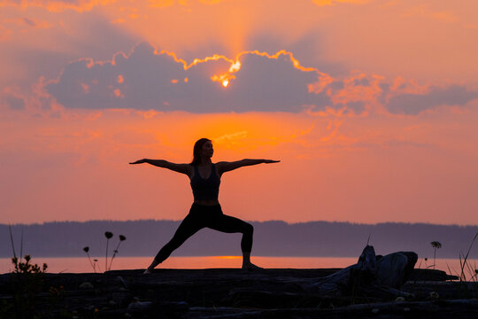 Silhouette of a person practicing yoga during a vibrant sunset on a rocky shoreline.