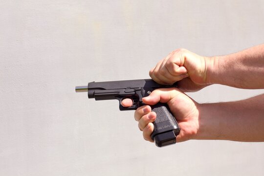 Person racking the slide of an airsoft gun against light gray wall.