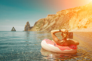 Woman laptop sea. Freelancer woman in sunglases floating on an inflatable big pink donut with a laptop in the sea. People summer vacation rest lifestyle concept