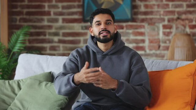 Professional couch sitting on sofa in comfort clothes while throwing hands to different sides and smiling at camera. Confident human giving examples of positive and negative outcomes of events.