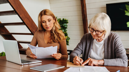 Senior woman with help of her daughter making bills at home