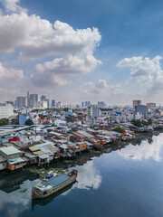 Obraz premium Vertical aerial shot of Ho Chi Minh City, Vietnam skyline from the canal between districts four and seven. Photo features boats on canal with the dramatic sky and buildings reflected on a sunny day. 