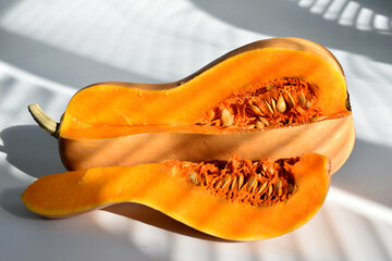 A ripe cut pumpkin with seeds lies on the table. The sun's rays fall on the pumpkin.