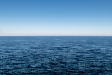 Fototapeta premium Endless ocean meeting the clear blue sky on horizon. Gentle waves on the surface water create a peaceful scene with no visible land, emphasizing solitude vastness.