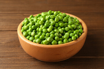 Fresh green peas in bowl on wooden table, closeup