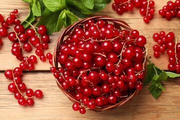 Fresh red currants in basket and mint on wooden table, flat lay