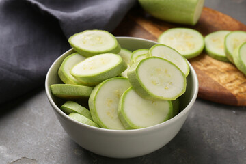 Fresh cut zucchinis in bowl on grey textured table, closeup