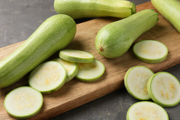 Board with fresh cut and whole zucchinis on grey textured table, closeup