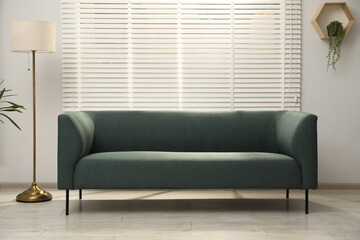 Comfortable couch, floor lamp and green plant near light wall indoors. Interior design