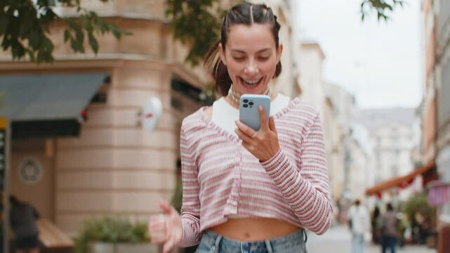 Oh my God Wow. Excited happy joyful winner young woman with teeth braces using smartphone looking at screen celebrating win receive good message news. Girl with mobile phone in urban street outdoors