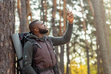 Black guy with backpack holding smartphone up, looking for gps in woods, got lost