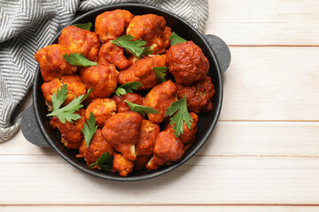 Baked cauliflower buffalo wings with parsley in baking dish on wooden table, top view