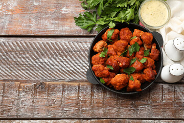 Baked cauliflower buffalo wings with parsley served on wooden table, flat lay. Space for text
