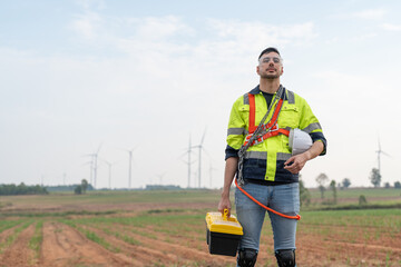 Male windmill engineer wearing uniform hold helmet safety standing at wind turbine farms for generating renewable energy.