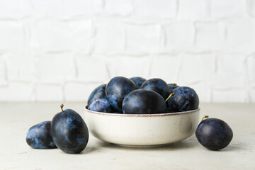 Ripe plums in bowl on light textured table