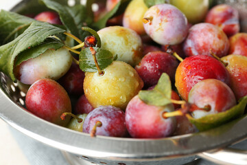 Ripe plums and leaves in colander on table, closeup