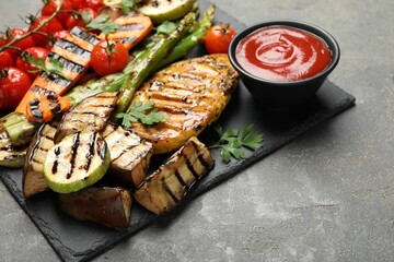 Delicious grilled vegetables and chicken breast served with sauce on grey table, closeup