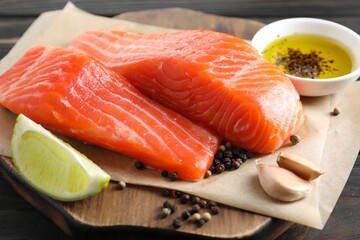 Pieces of fresh salmon, garlic, lime, oil and spices on wooden table, closeup