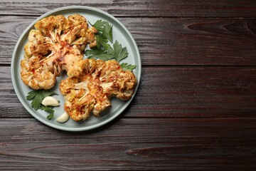 Delicious baked cauliflower steaks with garlic and parsley on wooden table, top view. Space for text