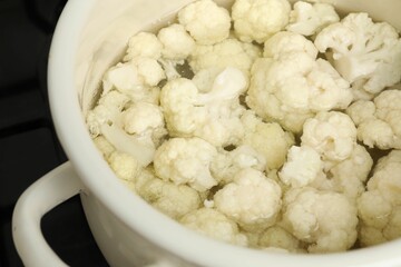 Cooking cauliflower. Florets in white pot with water on cooktop, closeup