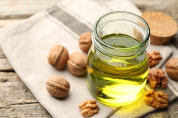 Cooking oil in jar and walnuts on wooden table, closeup. Space for text