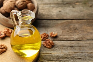 Cooking oil in jug and walnuts on wooden table, closeup. Space for text