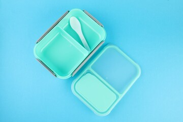 Empty plastic lunch box with cutlery on light blue background, top view