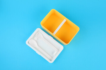 Empty plastic lunch box with cutlery on light blue background, top view