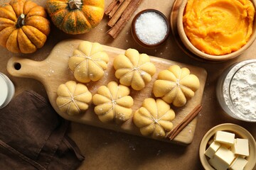 Raw pumpkin shaped buns and ingredients on brown table, flat lay