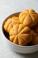 Tasty pumpkin shaped buns in bowl on grey table, closeup