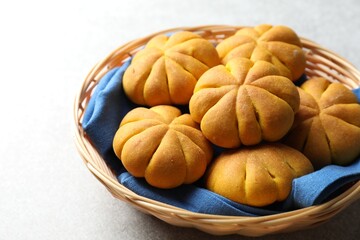 Wicker basket with tasty pumpkin shaped buns on light table, closeup