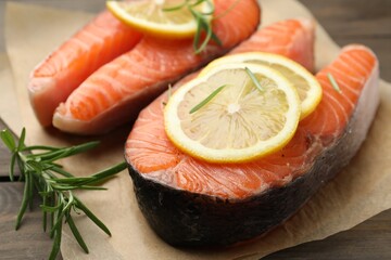 Fresh raw salmon steaks with rosemary and lemon on wooden table, closeup