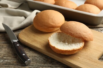 Fresh tasty buns and knife on wooden table, closeup