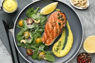 Tasty grilled salmon steak with lemon, sauce and salad served on grey textured table, flat lay