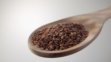 A close-up view of brown flax seeds piled on a wooden spoon against a white backdrop. The natural texture of the seeds and the simplicity of the background create a clean, minimalist visual focus.