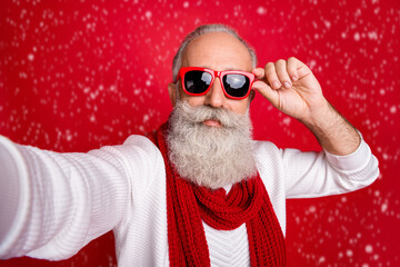 Fashion aged santa man making self photos wear sun specs knitted jumper isolated red background