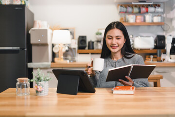 Fototapeta premium woman enjoys cozy moment at home, sipping coffee while reading notebook and using tablet. warm kitchen setting enhances relaxed atmosphere.