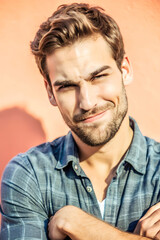 Obraz premium A man in his late 20s, raising one eyebrow with a smirk on his face. His arms are crossed, and his posture is relaxed but confident